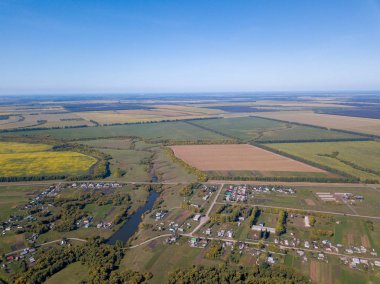 Yaz sezonunda köyün drone havadan görünümü. Çim tarlaları ve ağaçlar arasındaki evlerin ve çiftliklerin çatıları. Yerleşim de gölet kuş bakışı görünümü. Penza region, Russia.Pastoral kırsal peyzaj.