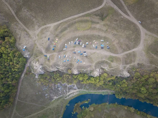 The turn of the river in valley with riversides covered by green forest and meadows and touristic camp with tents, cars and domes. Aerial top down view, drone shot. Russia, Vorgol river.