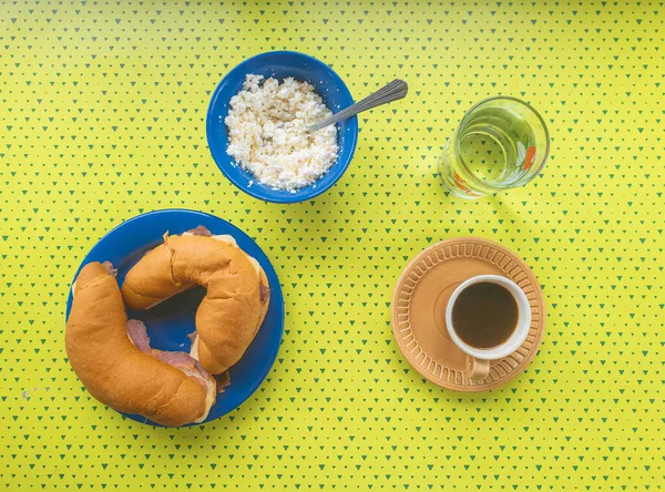 Süzme peynir, jambon ve peynirli simit, kahve ve saf su ile sağlıklı bir kahvaltı. Çanak çömlek ve çatal bıçaklı masa, kahvaltı için hazır. Üst alt görünüm. 