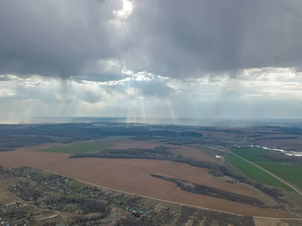Güneş ışınları ile dramatik bir gökyüzü tarımsal tarlalar, çayırlar ve ormanlarla dolu kırsal arazide bulutlar arasından geçiyor. İHA 'dan hava görüntüsü. Idyllic Avrupa yaz ülke manzarası.