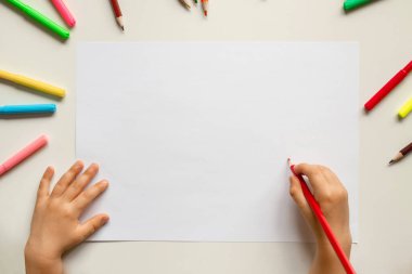 Çocuk elleri masada kalemlerle, beyaz kağıtlarla, okul aktiviteleriyle resim çiziyor.