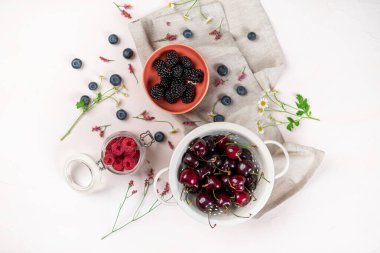 Yukarıdan pembe arka planda kiraz, böğürtlen ve yabanmersini kaseleri.