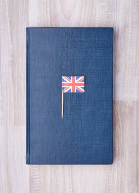 Kürdan üstte küçük İngiltere bayrağı ile ahşap masanın üzerinde yatan basit mavi defter atış yukarıdan