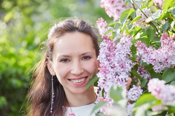 Young pretty woman with nice earrings posing near brunches of blooming lilac