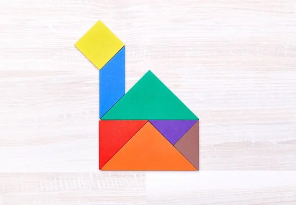 Flay lay of colorful tangram figures arranged in shape of boat on wooden table