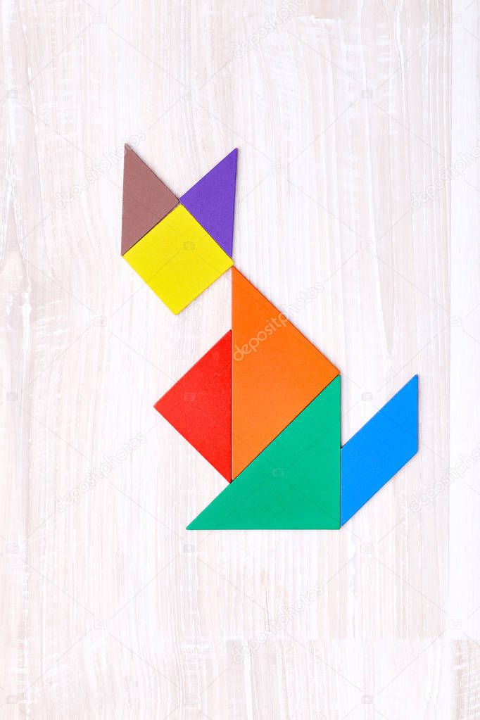 Flay lay of colorful tangram figures arranged in shape of cat on wooden table
