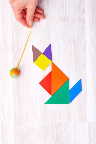 Flay lay of colorful tangram figures arranged in shape of cat that plays with ball on wooden table