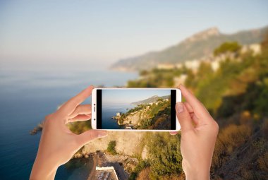Bir turist manzara fotoğrafını İtalya Amalfi kıyısında bir cep telefonuna şafak sırasında alıyor