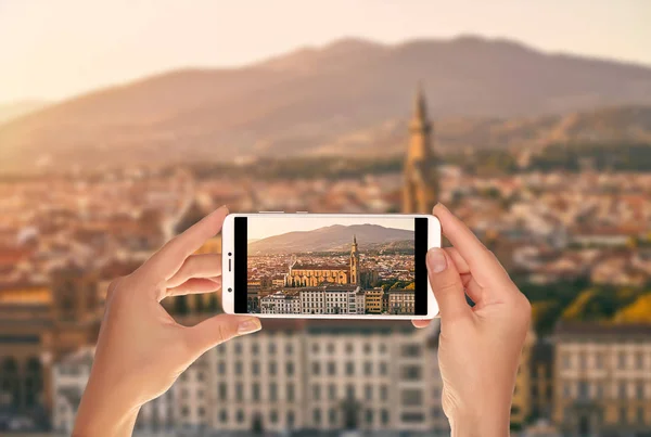 A tourist is taking a photo of panorama of Florence at sunset with the Basilica di Santa Croce (Basilica of the Holy Cross) illuminated by the setting sun on a mobile phone