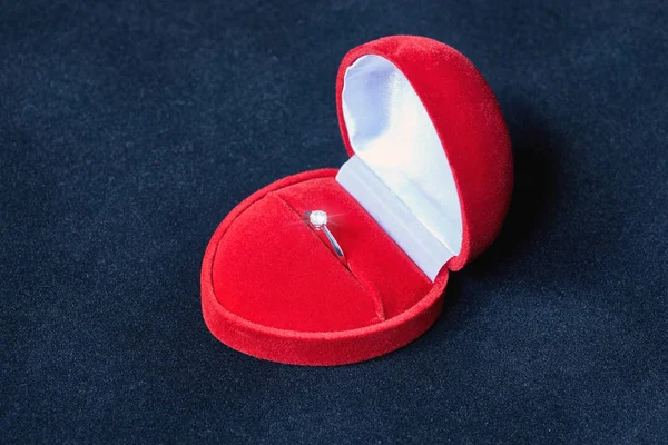 An engagement silver ring in a red box in the form of a heart with a shiny precious stone