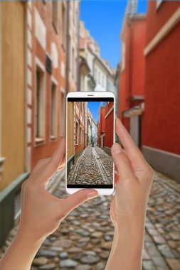 Bir turist bir fotoğraf dar bir Avrupa Riga'da eski şehir bir cep telefonu üzerinde kaldırım taşları ile sokak çekici