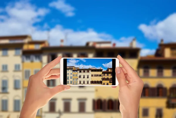 A tourist is taking a photo of facades of different old houses on Piazza de Pitti in Florence, Italy on a mobile phone