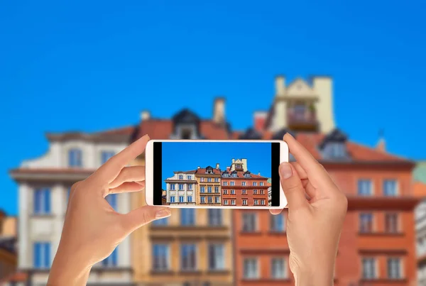 A tourist is taking a photo of facades of three buildings in the old town in Warsaw, Poland on a mobile phone