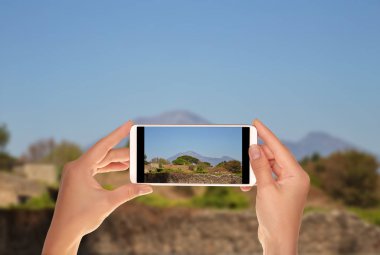 Bir turist bir güneşli gün yaz Vesuvius ile bir cep telefonu üzerinde arka planda savaşın manzara fotoğrafını alıyor
