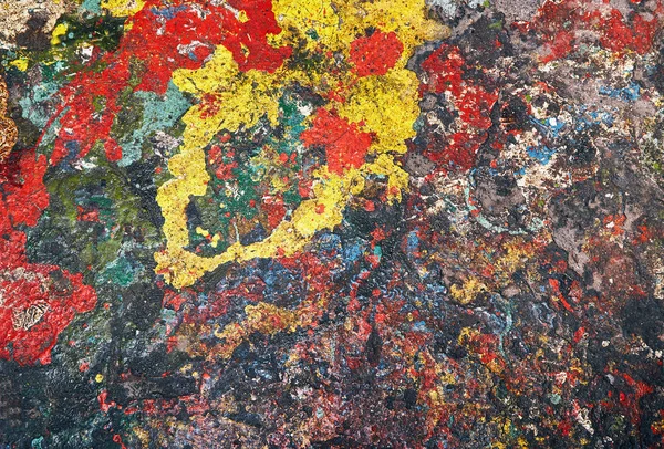 Spots of paint red, yellow, blue and other colors are randomly spilled on concrete and form an abstract background