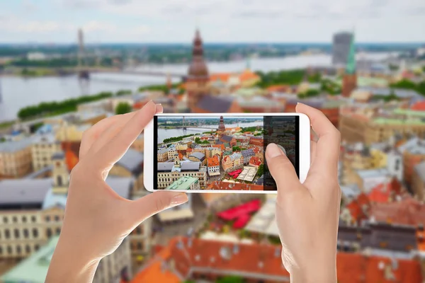 A man is making a photo of panorama of the city of Riga with tilt shift lens on a mobile phone