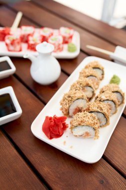 Beyaz tabak ve ahşap masa üzerinde suşi ruloları olan kompozisyon. Japon gıda konsepti