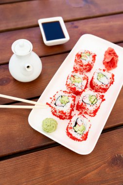 Beyaz tabak ve ahşap masa üzerinde suşi ruloları olan kompozisyon. Japon gıda konsepti
