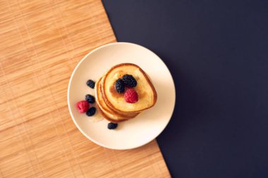 Beyaz tabakta ahududu, dut ve bal ile krep. Üst görünüm