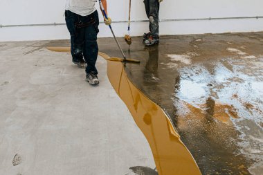 Bir işçi fünyeyi beton zemine uygular. Epoksi reçinesi projesi.