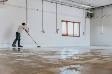 Bir işçi fünyeyi beton zemine uygular. Epoksi reçinesi projesi.