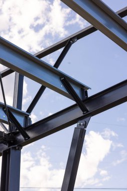 İnşaat halindeki bir binayı destekleyen çelik çerçeve yapısı ve arkasında mavi gökyüzü ve beyaz bulutlar var.
