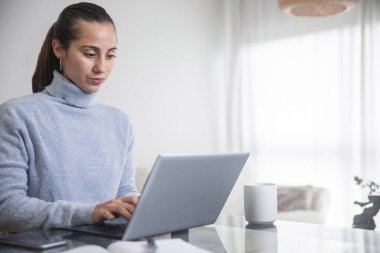 Bir kadın, oturma odasında bilgisayarıyla evden işe koşturuyor.