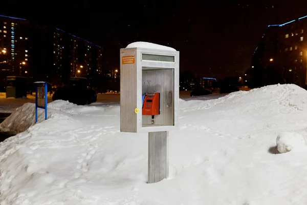 Metalik gri telefon kulübesi, karda kırmızı telefon, kışın şehir gecesi.