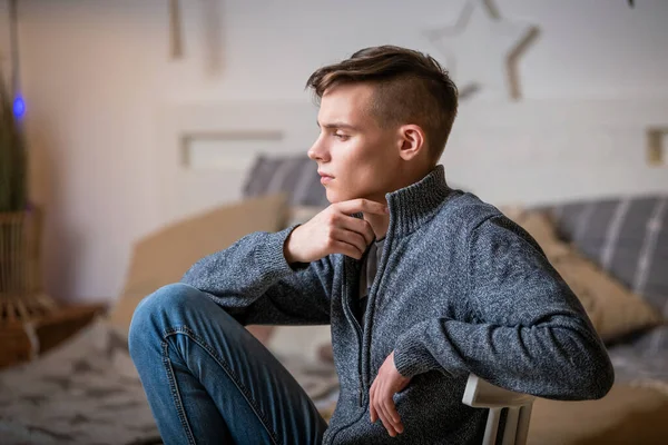Cute young man with a pensive look sits alone indoors in a rustic style