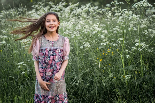 A girl in a patchwork dress in a rustic style walks in nature in the summer among tall wildflowers, her hair flutters in the wind