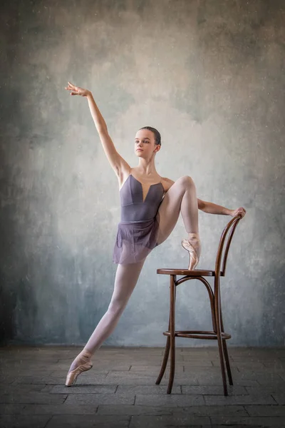 graceful ballet dancer in a light lilac suit and pointe shoes against a gray wall. Dance, grace, artist, contemporary, movement, action and freedom of movement concept.