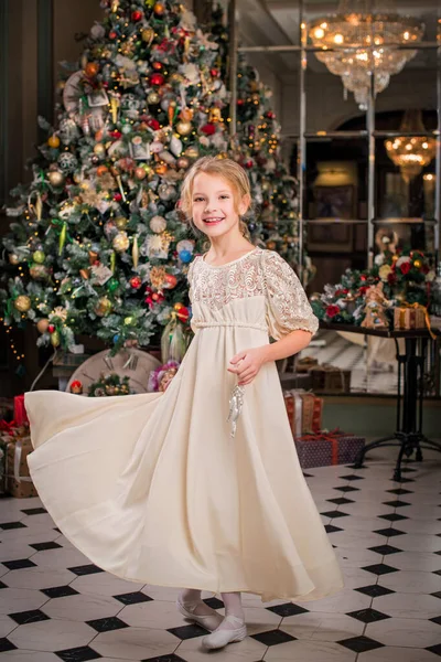 well-dressed little girl in a beautiful dress is dancing around the Christmas tree with a Christmas tree decoration in her hands