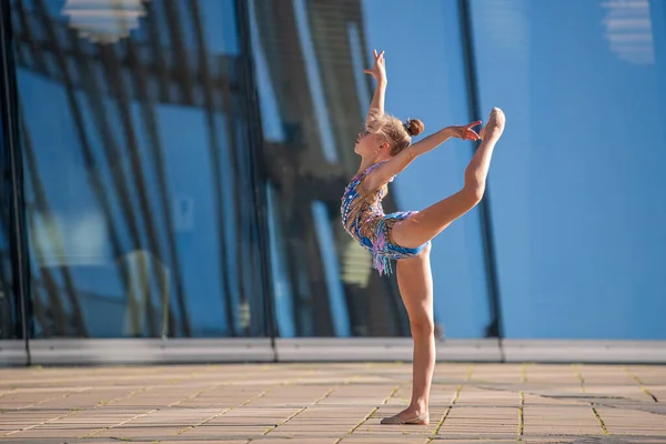 school-age girl gymnast in a beautiful blue suit performs an exercise without an apparatus. Frozen in a complex graceful pose.