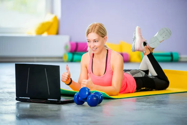 young woman trainer conducts workout online in front of laptop in the gym