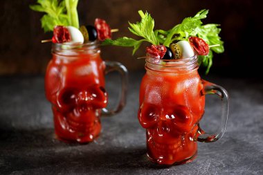 Kereviz çubukları, pembe tuz, limon ve konserve sebze lerden kanepeler ile cam kafatası Bloody Mary kokteyl. Cadılar Bayramı içkisi. 