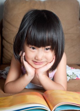 Kitap okurken gülümseyen Asyalı küçük kız 