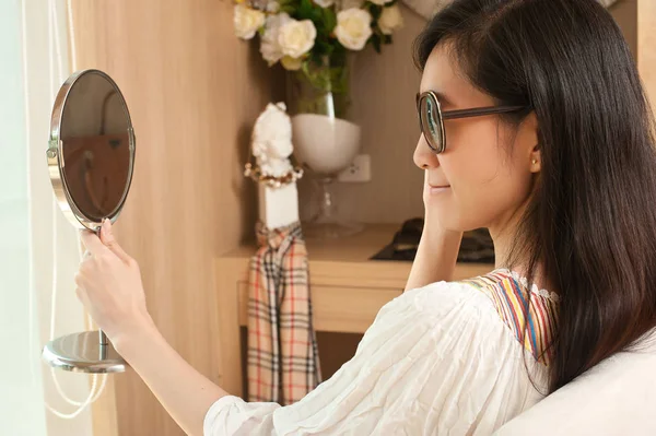 Young asian woman looking at the mirror while trying glasses.