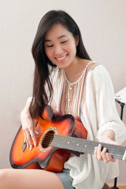 Müzik odasında oturma ve gitar ve eğlence kavramı oynamak gülümseyen Asyalı güzel kız.
