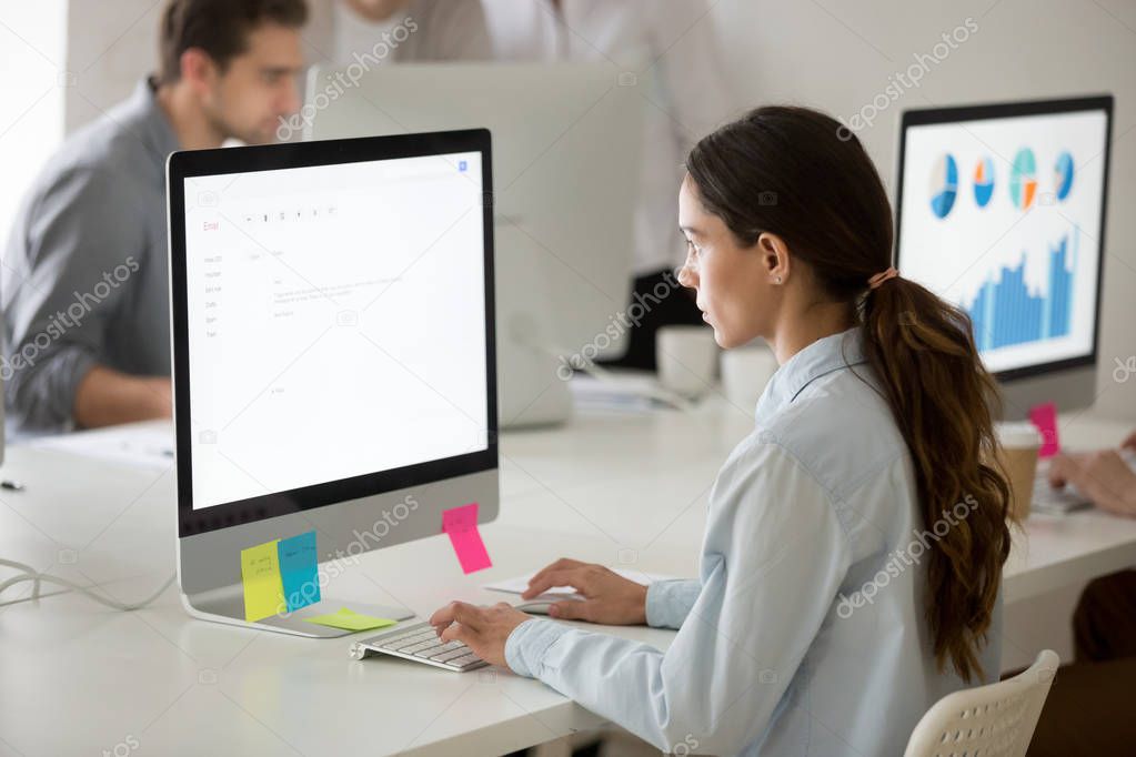 Serious girl intern focused on writing email working on computer