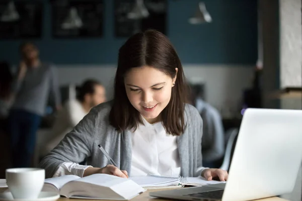 Smiling girl studying in cafe writing notes in exercise book — Stock Photo, Image