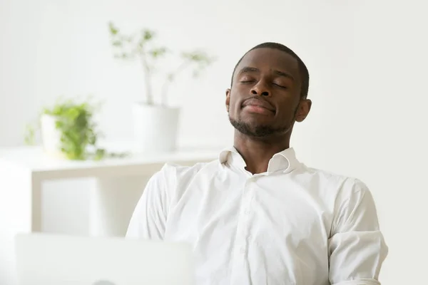 Satisfied African American worker meditating at workplace managi