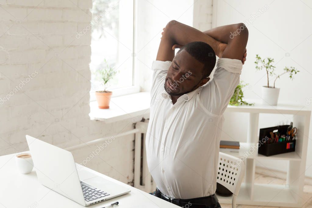Exhausted black worker doing office gymnastics in chair at workp