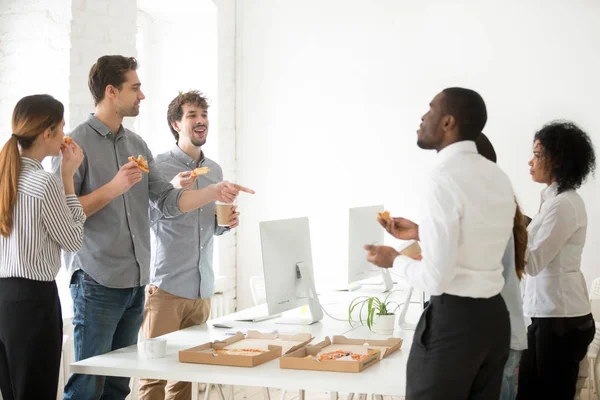 Positive diverse team eating pizza and chatting at workplace