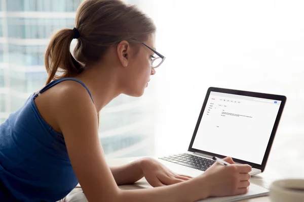 Vrouw in bril kijken laptop scherm, het maken van notities. — Stockfoto