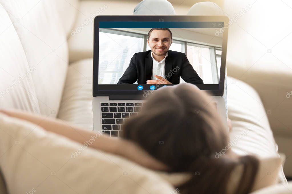 Woman lying on sofa chatting with boyfriend via video call.