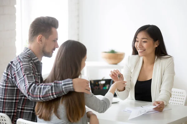 Smiling broker giving keys from first house to millennial couple — Stock Photo, Image