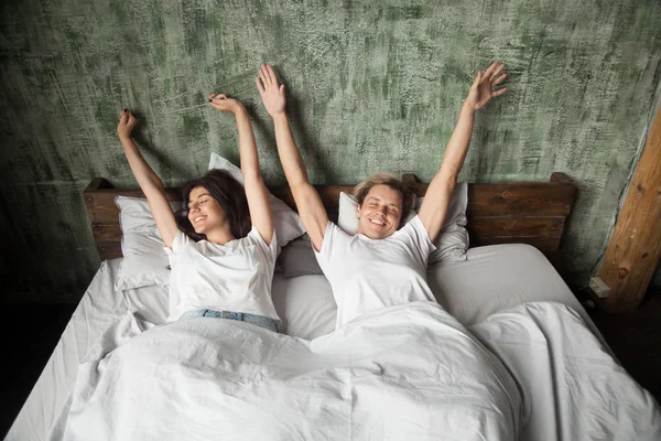Šťastný mladý pár vzpaženy v posteli po probuzení — Stock fotografie
