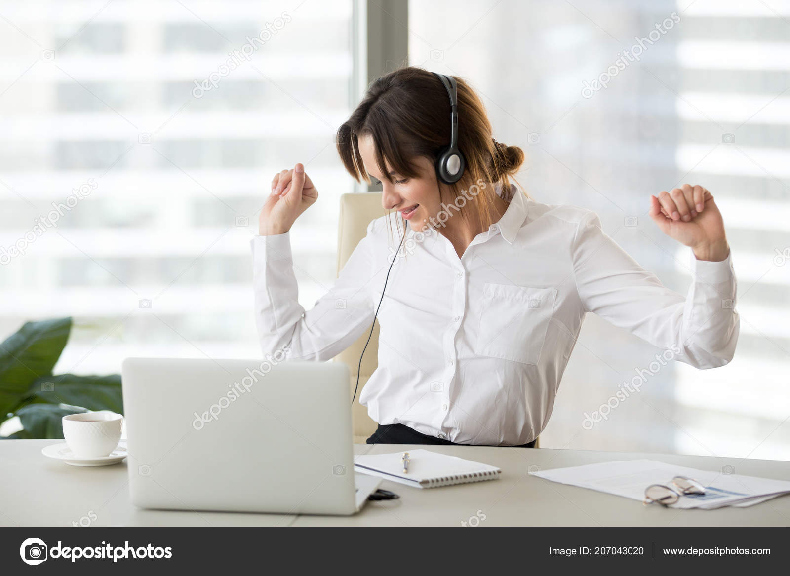 Happy Female Worker Listening To Music Dancing In Office Chair