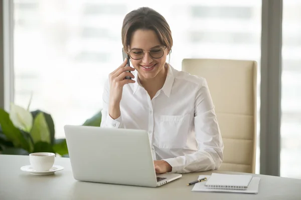 Улыбающаяся деловая женщина разговаривает по телефону во время работы за ноутбуком — стоковое фото