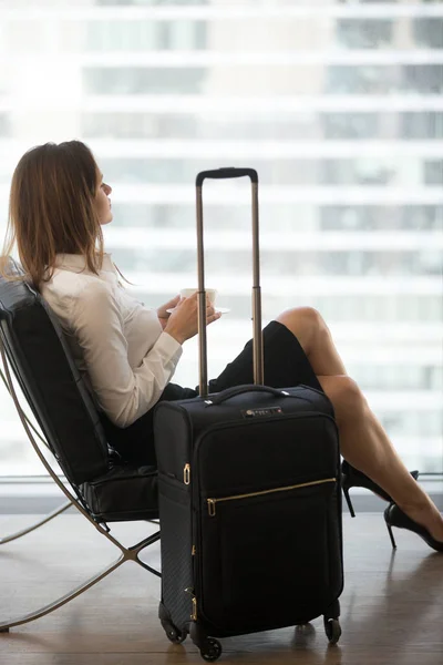 Задумчивая женщина пьет кофе в ожидании рейса в аэропорту — стоковое фото